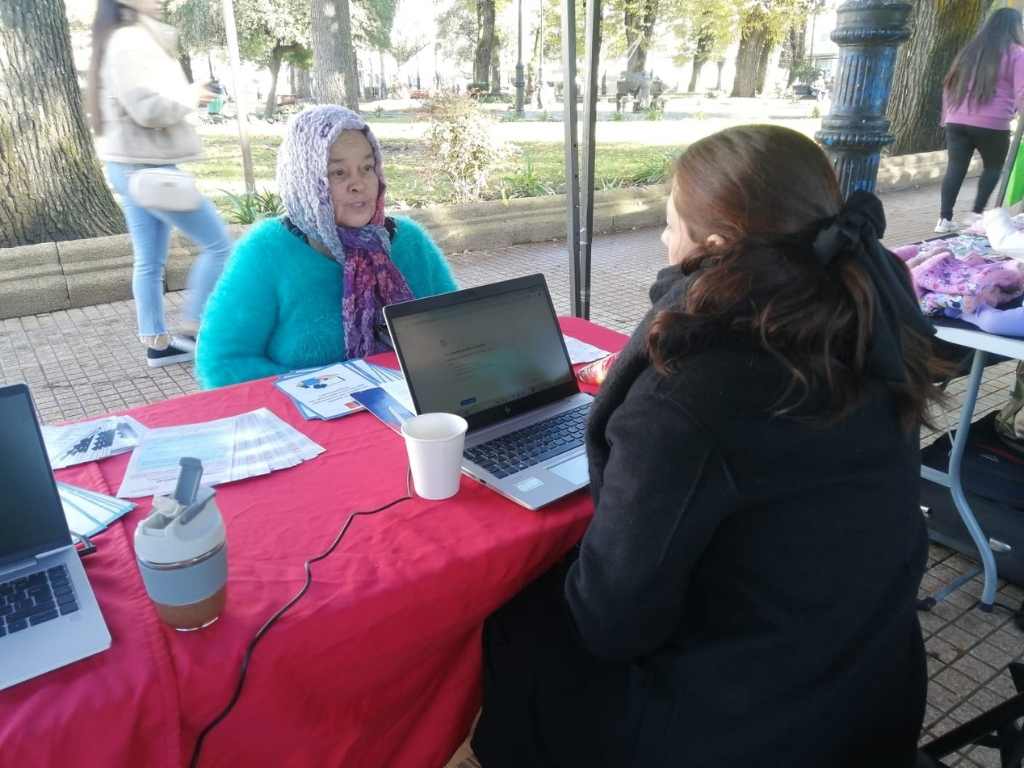 Funcionaria D.R Ñuble entrega información a persona migrante en feria de servicios públicos.